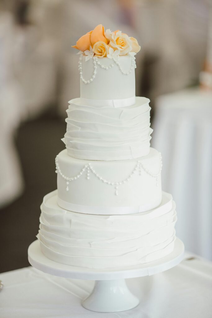 A sophisticated three-tier white wedding cake adorned with peach roses and pearl decorations.